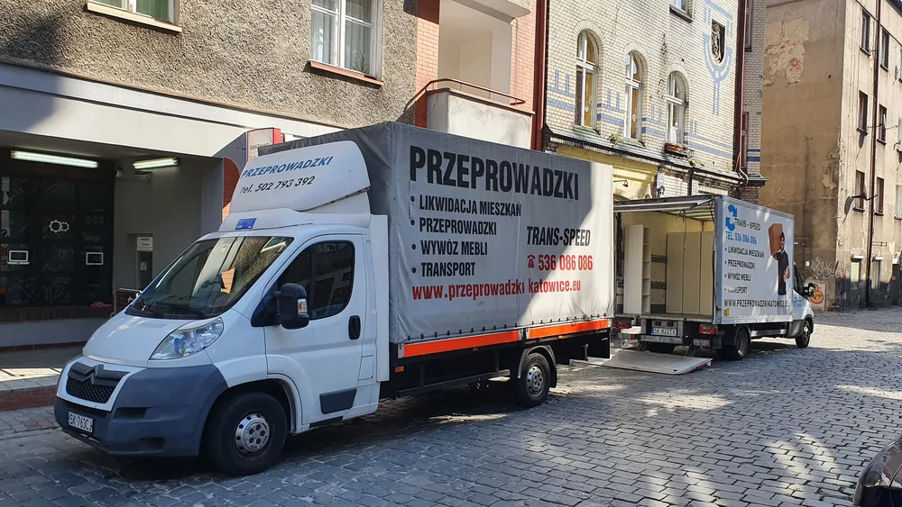 Dwa samochody firmy podczas przeprowadzki na wąskiej ulicy