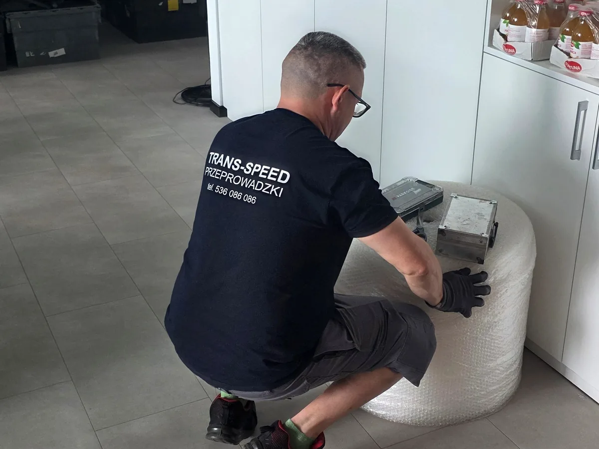 Pracownik Trans-Speed rozkręca szafkę wkrętarką, mebel oparty na folii zabezpieczającej
